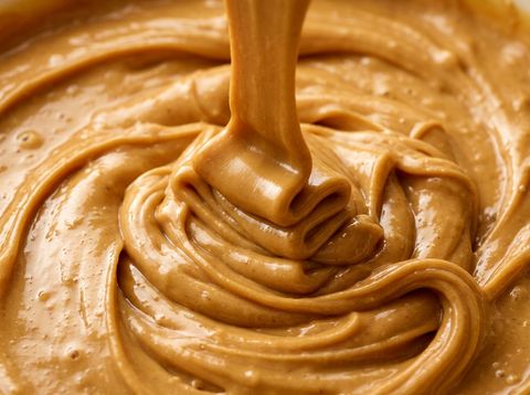 Glossy golden peanut butter swirling in thick creamy ribbon folds
